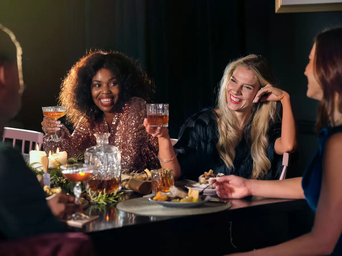Amigas rindo e brindando numa mesa durante um jogo de beber
